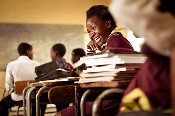 A Happy young South African girl (from the Xhosa tribe) works on her studies and jokes with her friends at at an old worn desk in a class room in the Transkei region of rural South Africa.